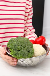 Photo of Woman holding colander with fresh vegetables at white marble table, closeup