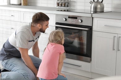 Photo of Little daughter and father sitting near oven in kitchen