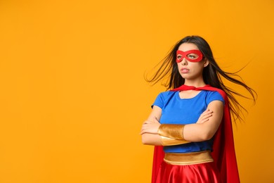 Photo of Confident young woman wearing superhero costume on orange background, space for text