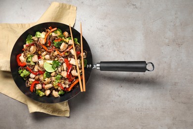 Photo of Stir-fry. Tasty noodles with meat in wok and chopsticks on grey textured table, top view