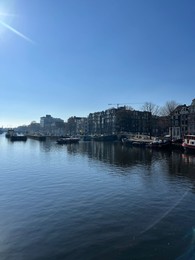 Photo of Amsterdam, Netherlands - March 01, 2023: Picturesque view of river embankment with moored boats in city under blue sky