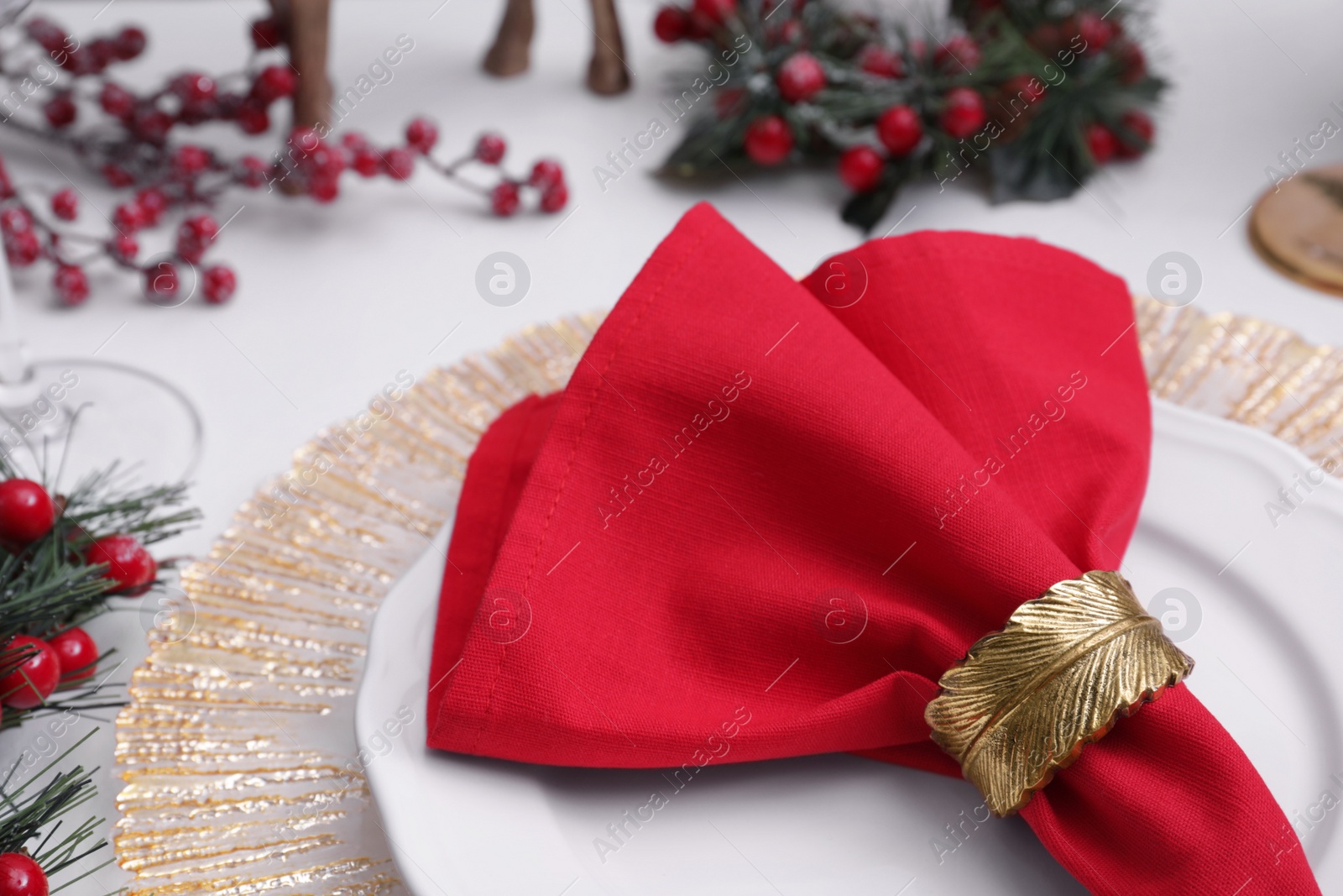 Photo of Plates and red fabric napkin with decorative ring on white table, closeup