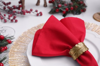 Plates and red fabric napkin with decorative ring on white table, closeup