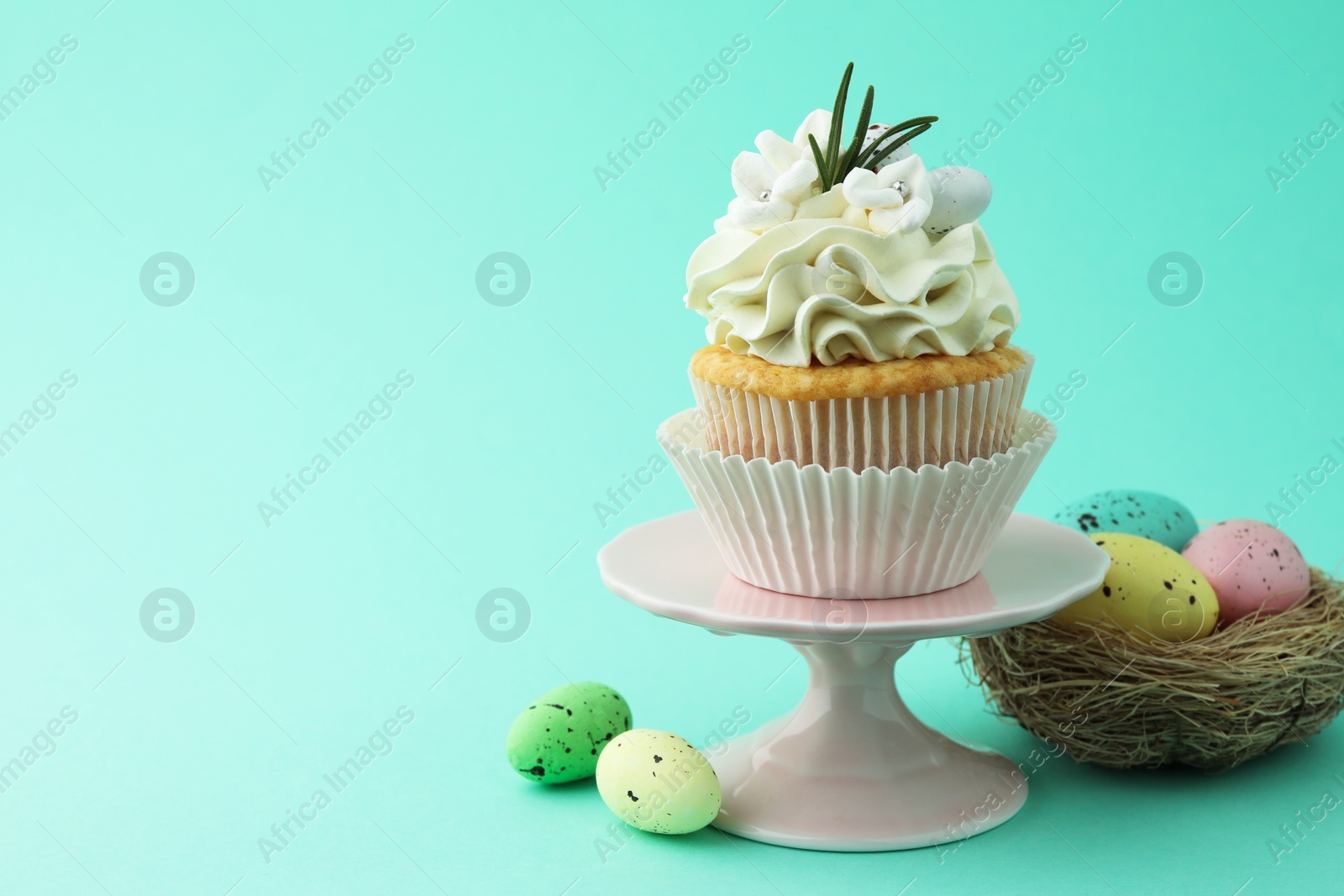 Photo of Tasty Easter cupcake with vanilla cream and festive decor on turquoise background, space for text