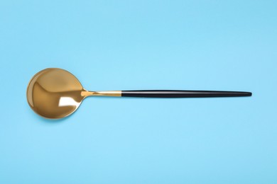 Photo of One shiny golden spoon on light blue background, top view