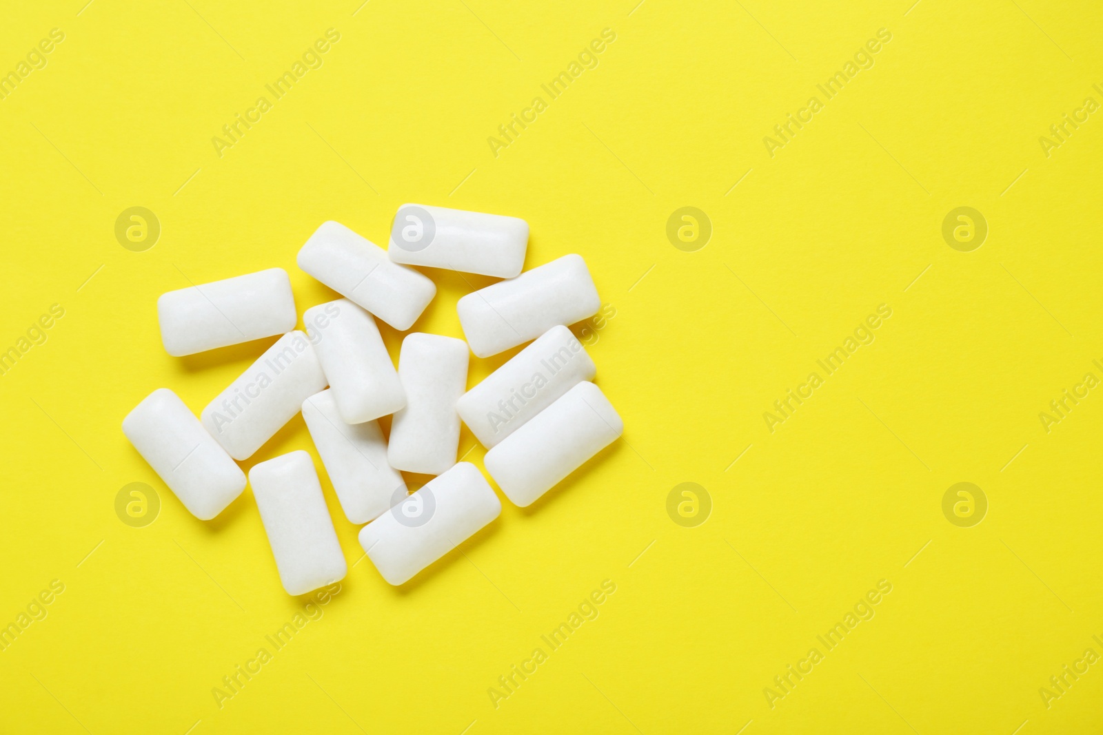 Photo of Tasty white chewing gums on yellow background, flat lay. Space for text