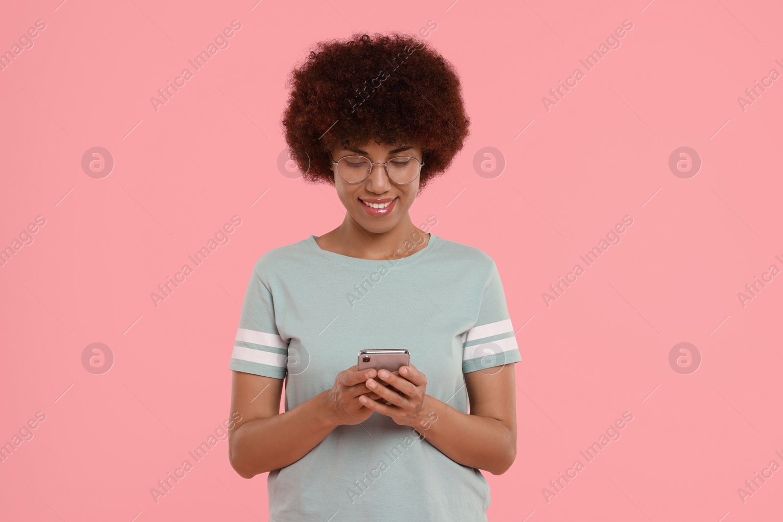 Photo of Young woman in eyeglasses using smartphone on pink background