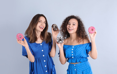 Beautiful young women with donuts on light grey background