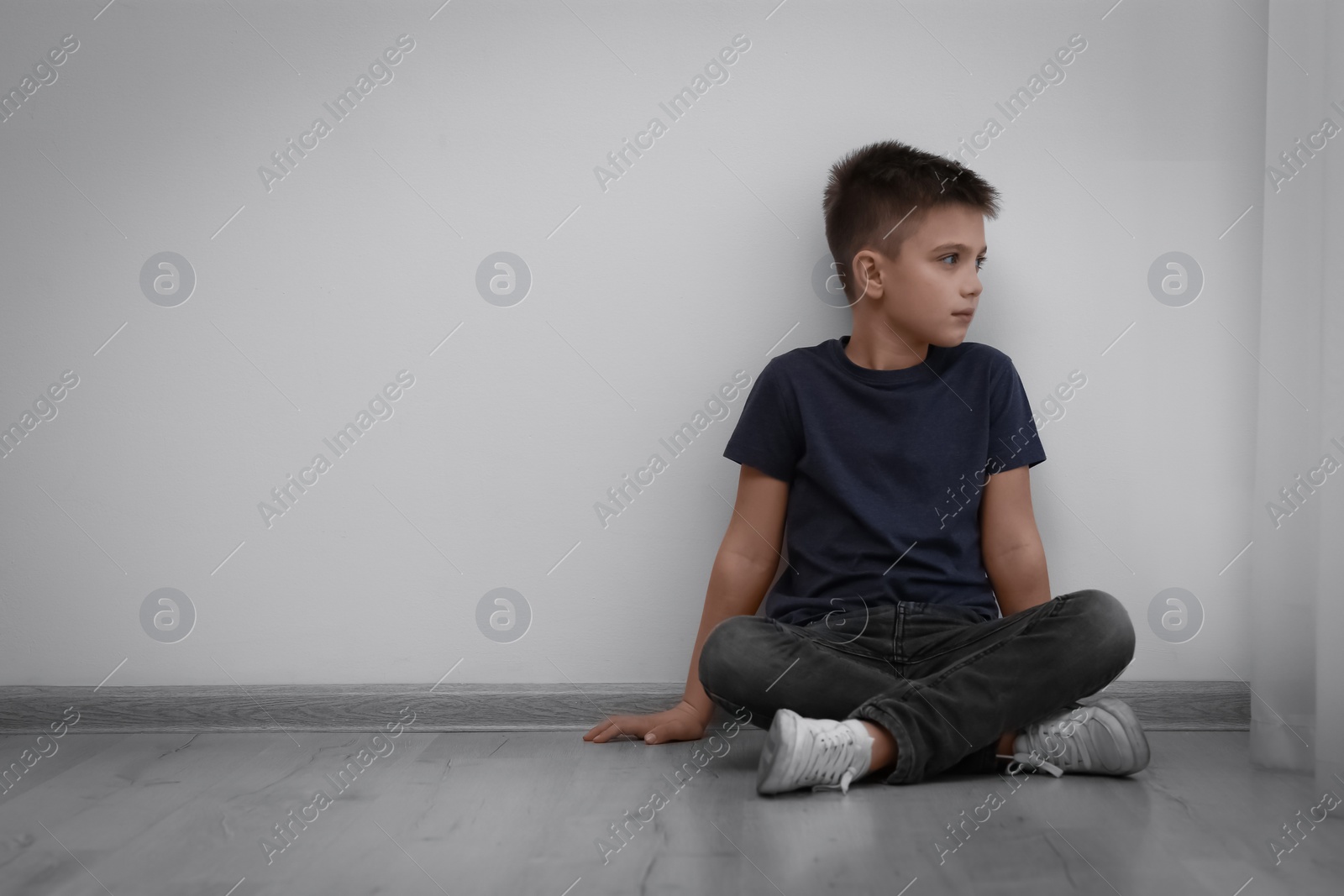 Photo of Sad little boy sitting on floor indoors, space for text. Child in danger