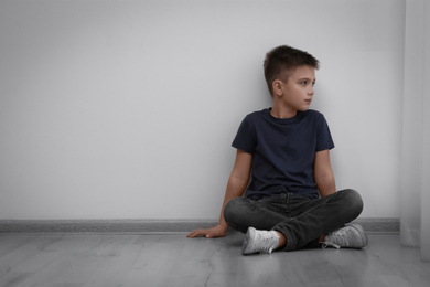 Sad little boy sitting on floor indoors, space for text. Child in danger