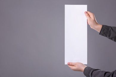 Man holding sheet of paper on grey background, closeup. Mockup for design