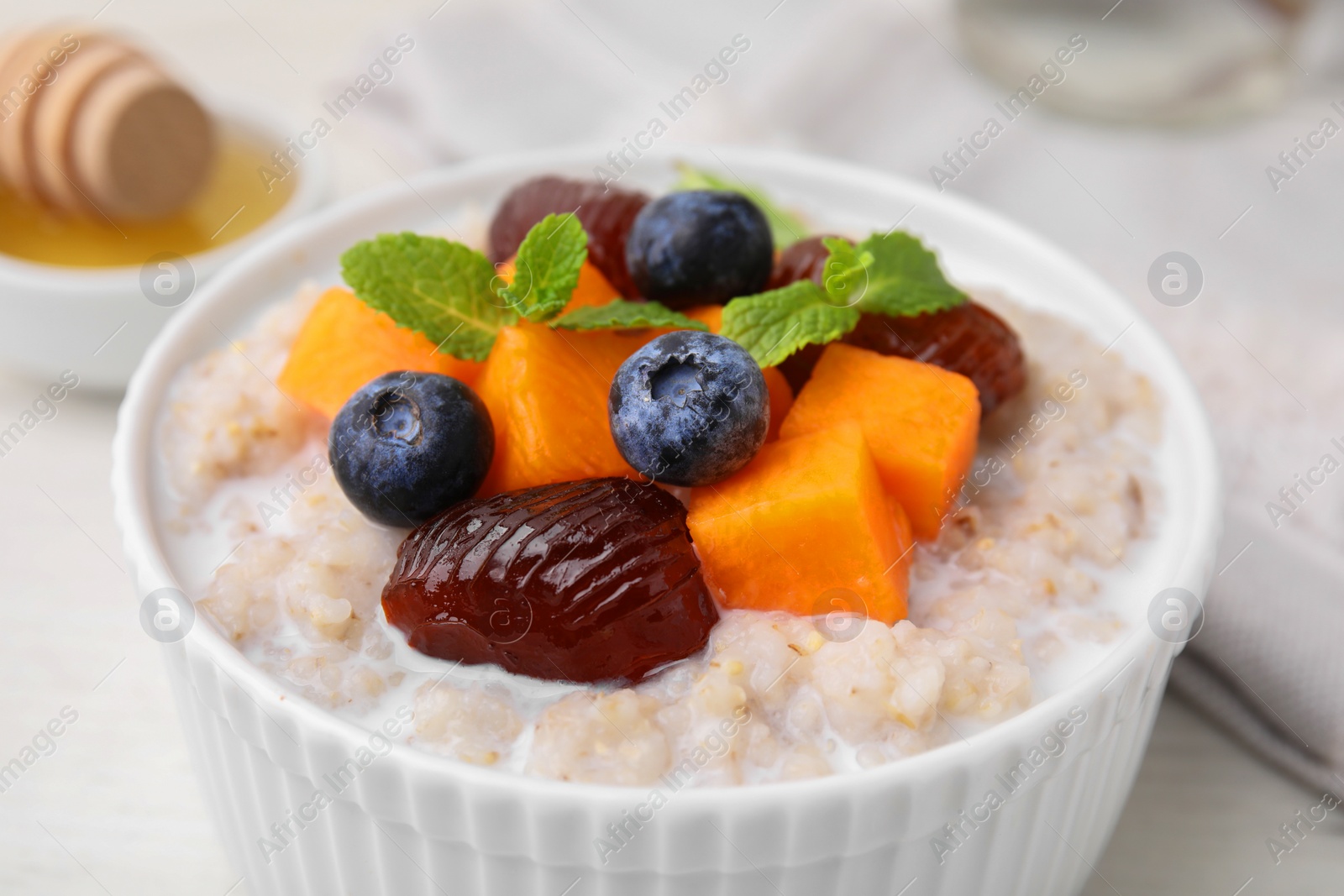Photo of Delicious barley porridge with blueberries, pumpkin, dates and mint in bowl on white table, closeup