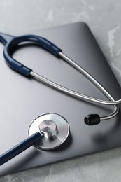 Modern laptop and stethoscope on grey table