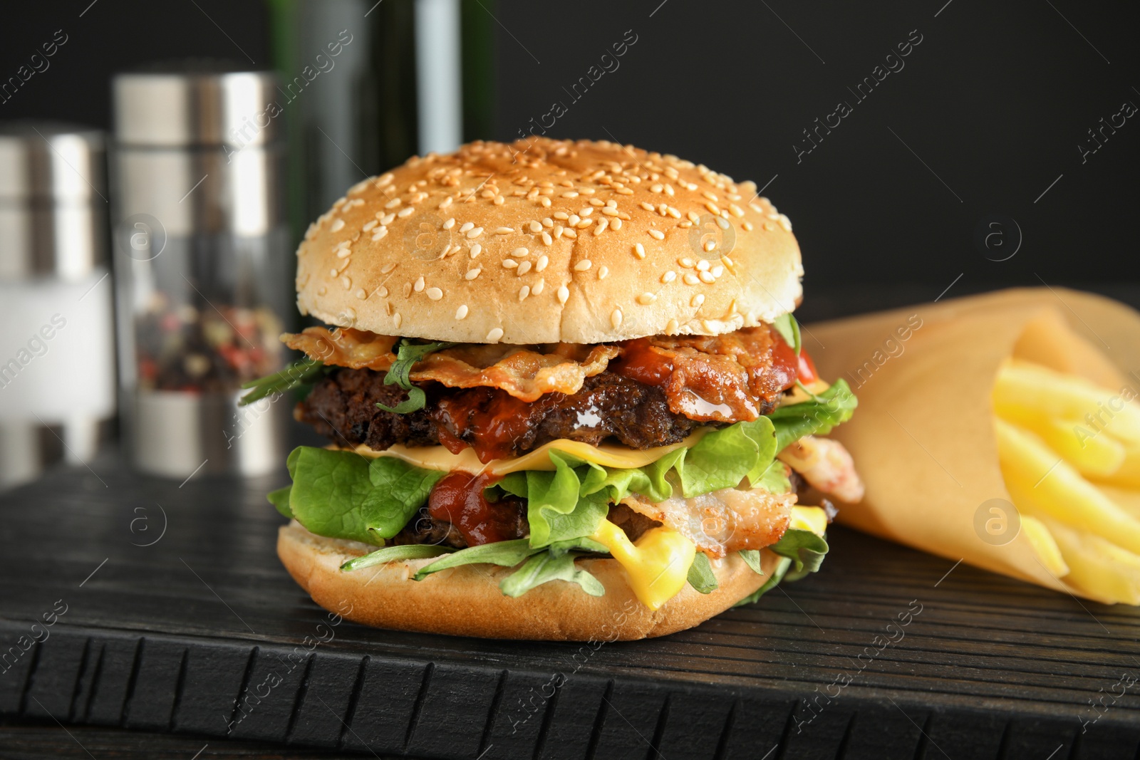 Photo of Tasty burger with bacon and French fries on board