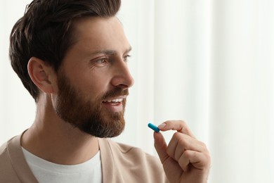 Handsome man taking pill indoors, space for text
