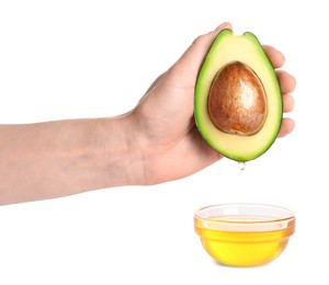 Photo of Woman holding half of avocado with essential oil dripping into glass bowl on white background, closeup