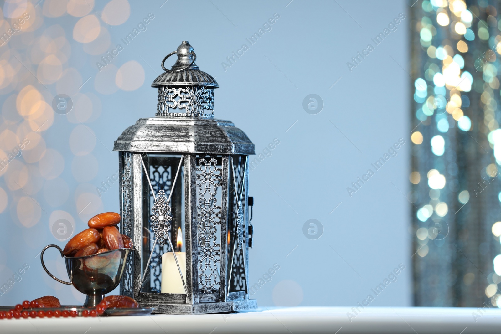 Photo of Arabic lantern, misbaha and dates on table against blurred lights, space for text