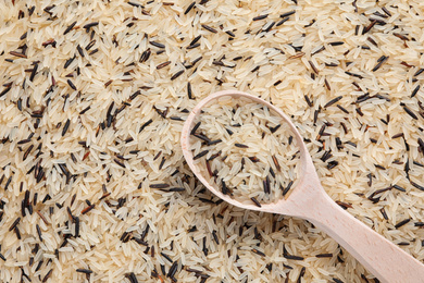 Mix of brown and polished rice with wooden spoon, top view. Space for text