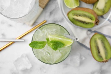 Glass of refreshing drink with lime and cut kiwi on white table, flat lay
