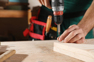 Photo of Professional carpenter twisting screw with drill at workbench, closeup. Space for text
