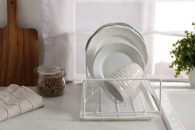 Drainer with different clean dishware and cup on light table indoors