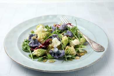 Photo of Delicious salad with cauliflower and pumpkin seeds served on white tiled table, closeup