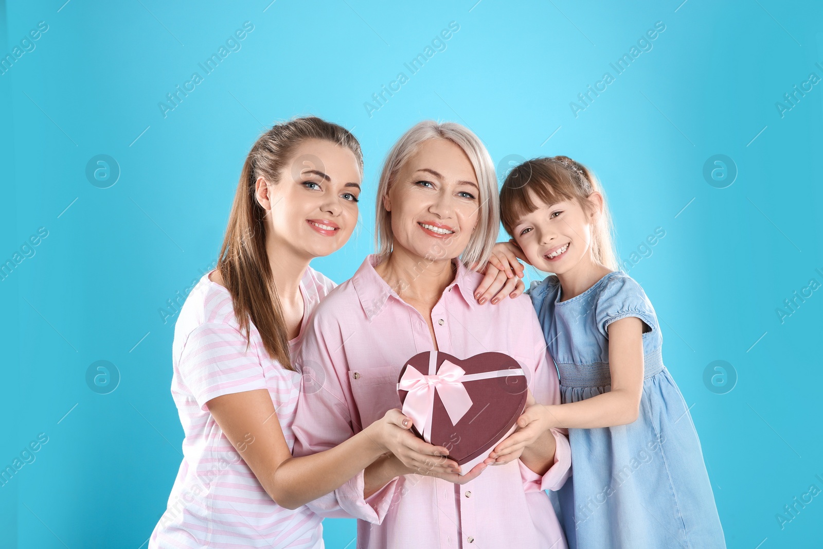 Photo of Beautiful mature lady, daughter and grandchild with gift on color background. Happy Women's Day