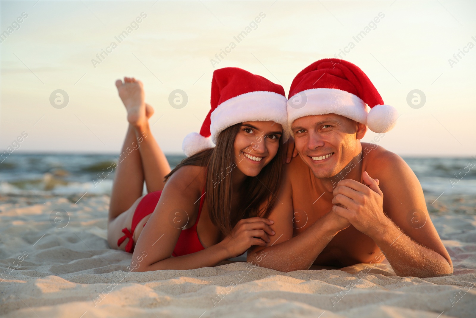 Photo of Happy couple with Santa hats together on beach. Christmas vacation