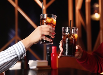 Photo of Young couple with glasses of refreshing cola at table indoors, closeup