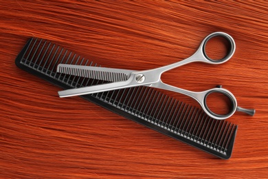 Photo of Thinning scissors and comb on red hair, top view. Hairdresser service