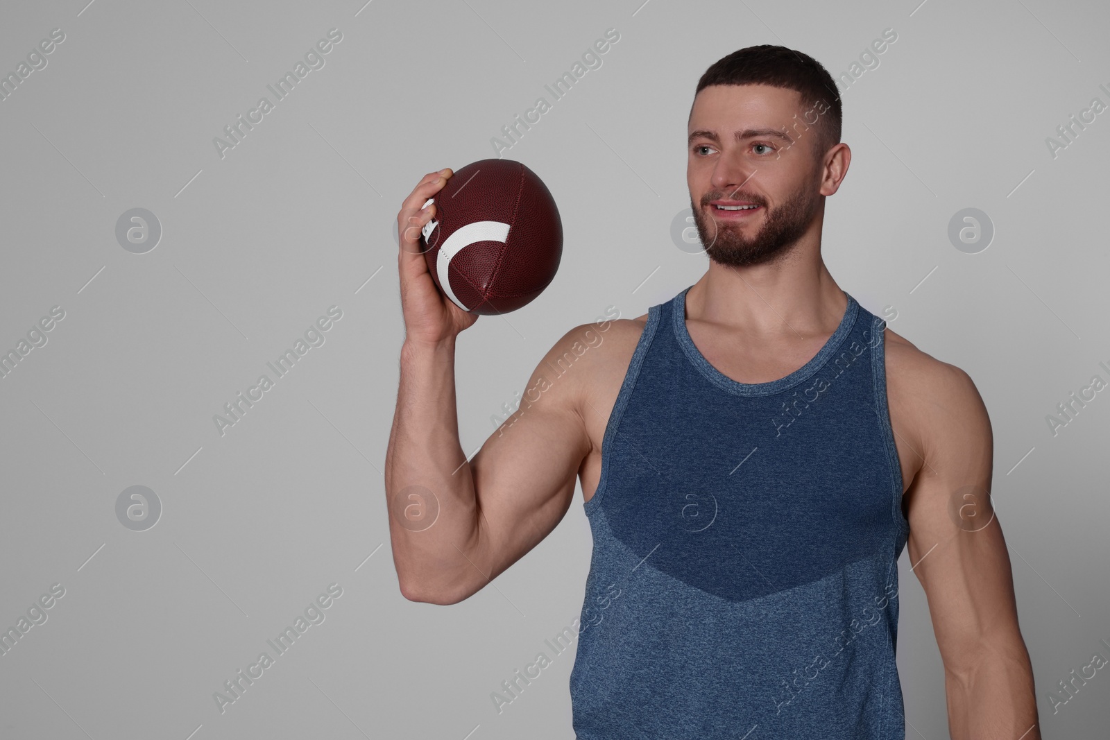 Photo of Athletic young man with American football ball on light grey background. Space for text