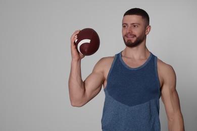 Athletic young man with American football ball on light grey background. Space for text