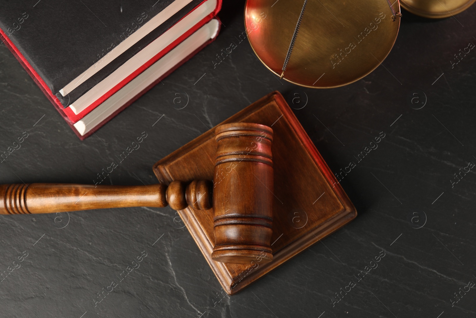 Photo of Wooden gavel, sound block and books on dark textured table, flat lay