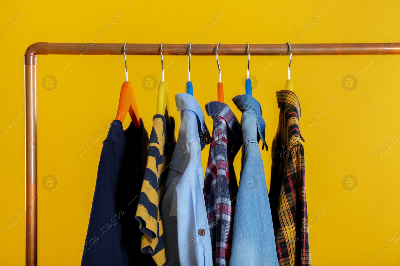 Photo of Rack with stylish children clothes on yellow background, closeup