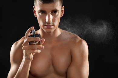 Photo of Handsome young man spraying perfume on black background