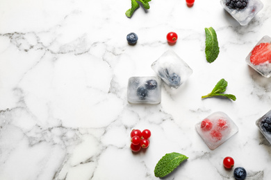 Photo of Ice cubes with different berries and mint on white marble table, flat lay. Space for text