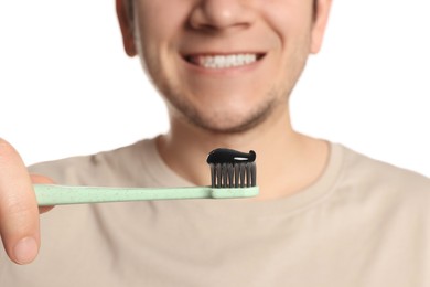 Photo of Man holding toothbrush with charcoal toothpaste on white background, closeup