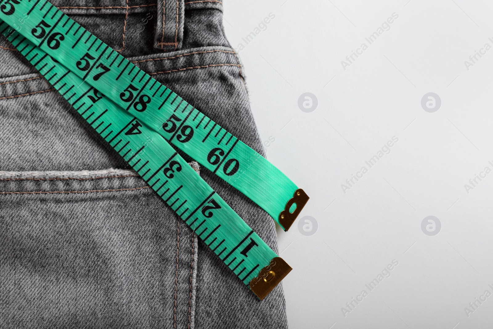 Photo of Jeans with measuring tape on light grey background, top view and space for text. Weight loss concept