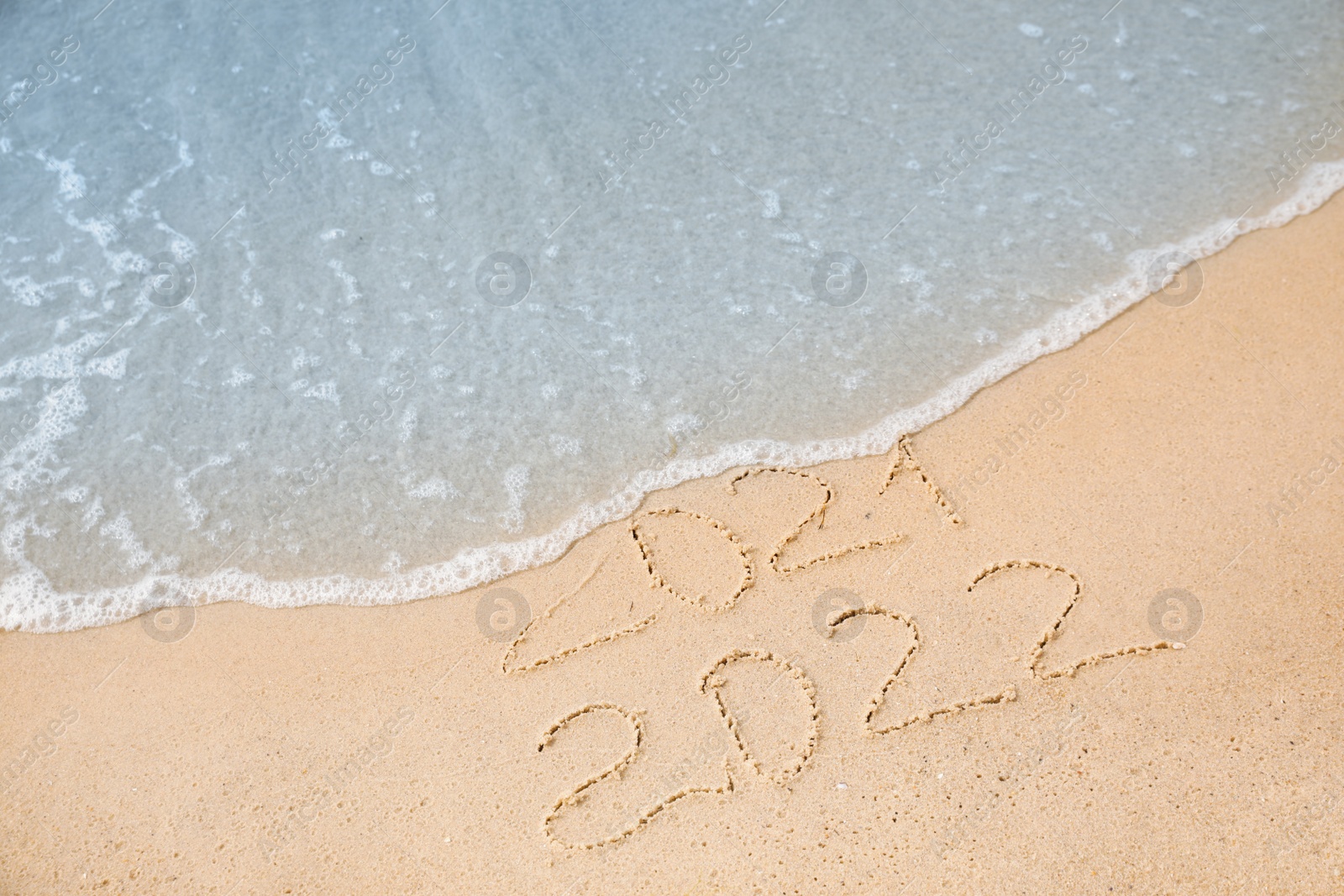 Photo of Dates written on sandy beach. 2021 washed by sea wave as New 2022 Year coming