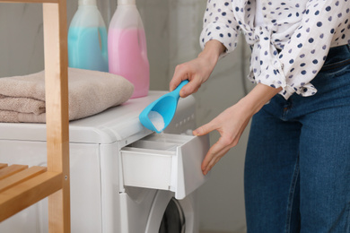 Photo of Woman pouring laundry detergent into washing machine drawer in bathroom, closeup