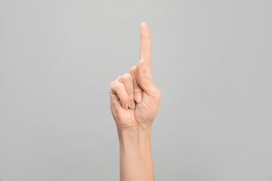 Woman showing number one on grey background, closeup. Sign language