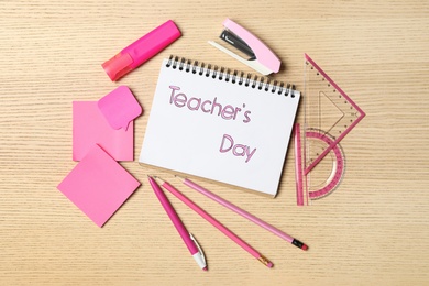 Notebook with words TEACHER'S DAY and set of pink stationery on wooden table, flat lay