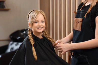 Professional hairdresser braiding girl's hair in beauty salon