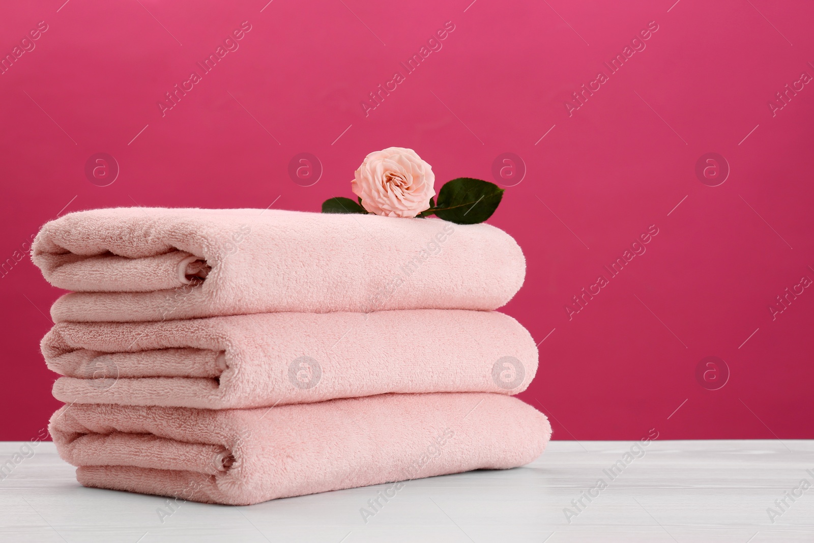 Photo of Stack of soft clean towels with beautiful flower on table against color background. Space for text