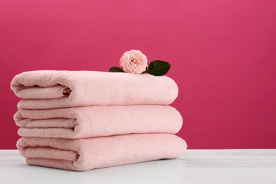 Stack of soft clean towels with beautiful flower on table against color background. Space for text