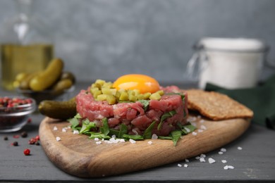 Photo of Tasty beef steak tartare served with yolk, pickled cucumber and other accompaniments on grey wooden table