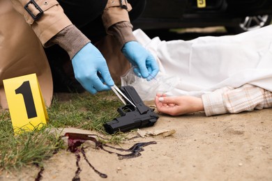 Photo of Investigator in protective gloves working at crime scene with dead body outdoors, closeup