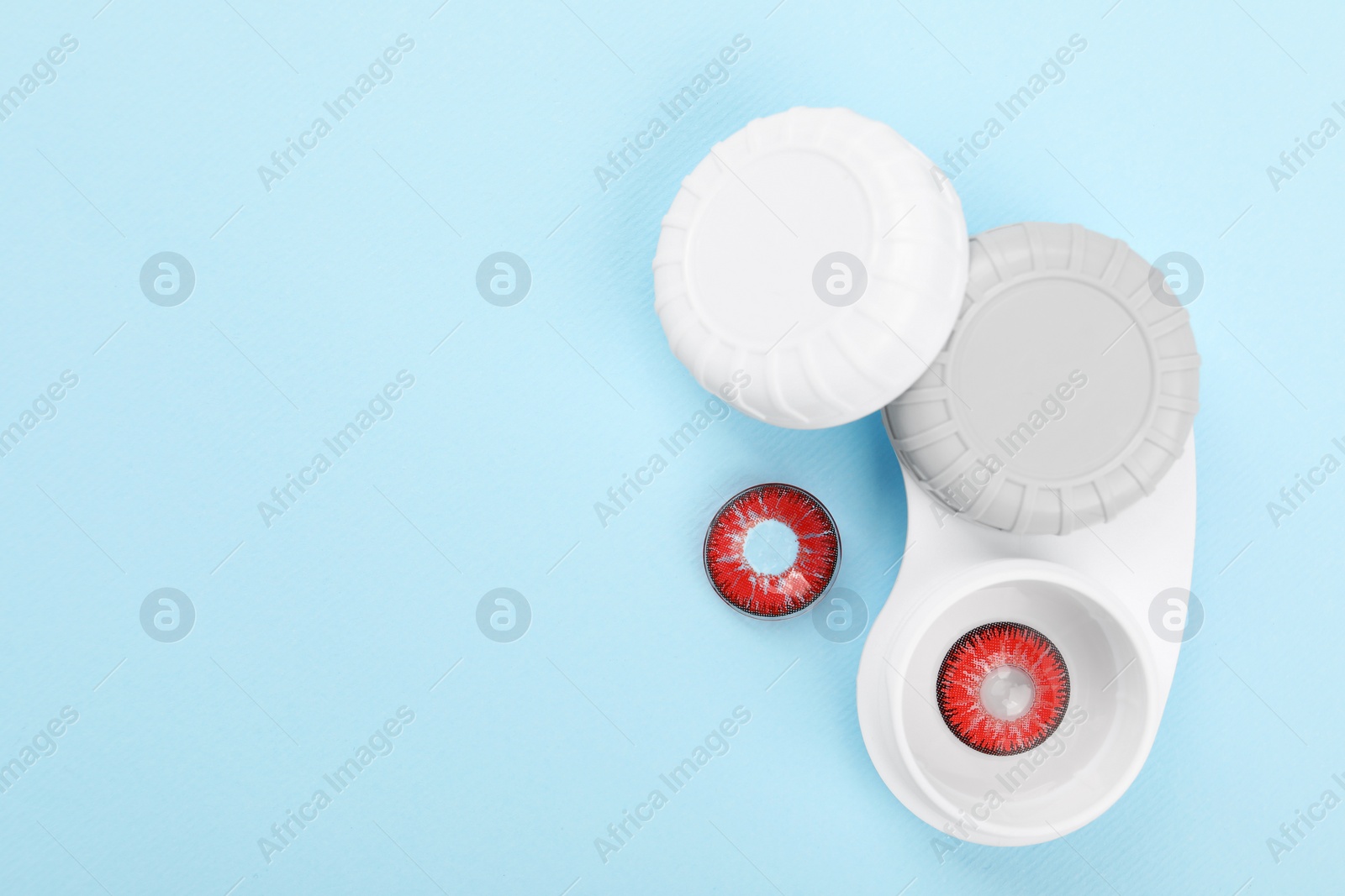 Photo of Case with red contact lenses on light blue background, flat lay. Space for text