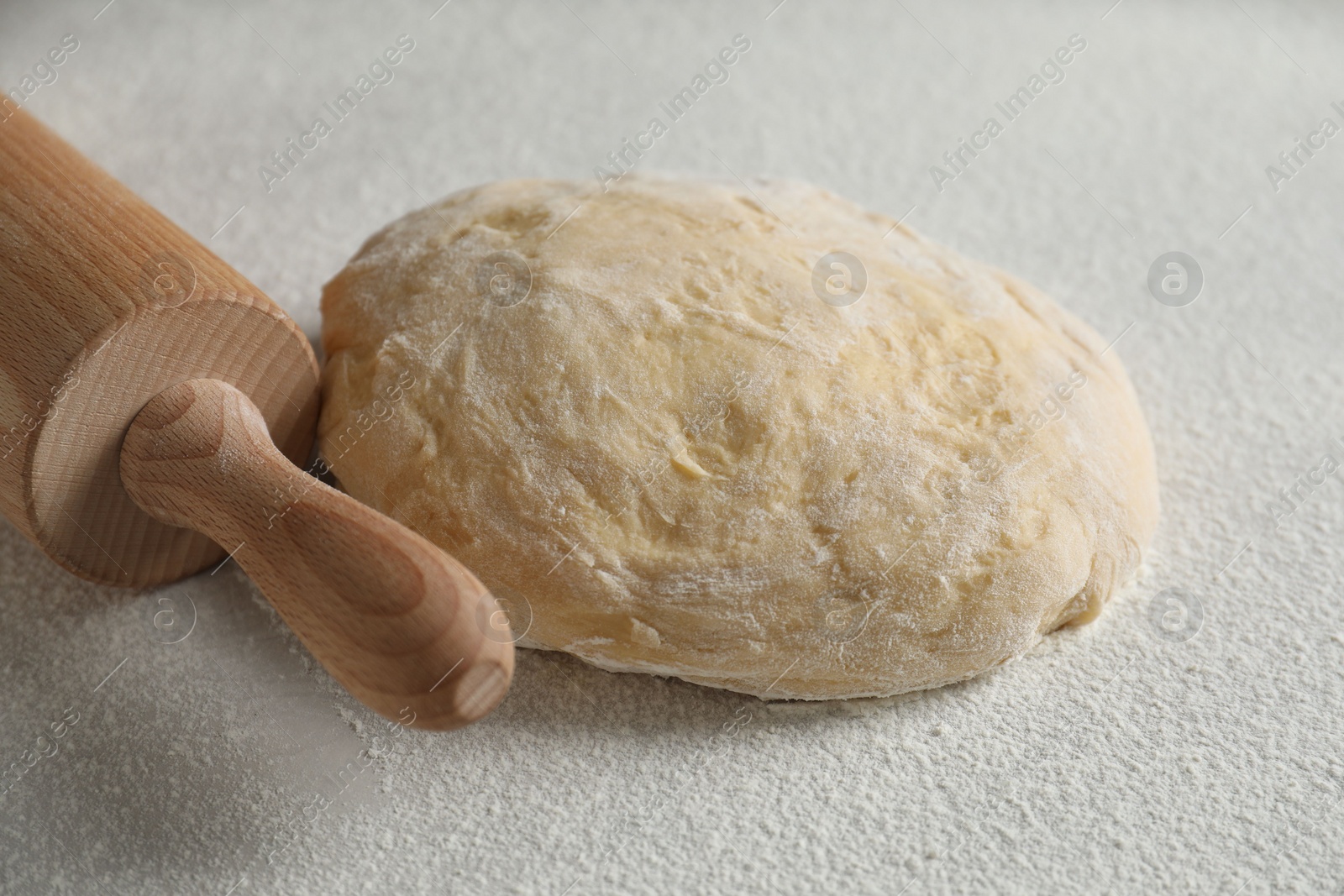 Photo of Raw dough and rolling pin on white table, closeup