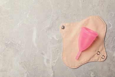Photo of Menstrual cup and cloth pad on grey background, top view. Space for text